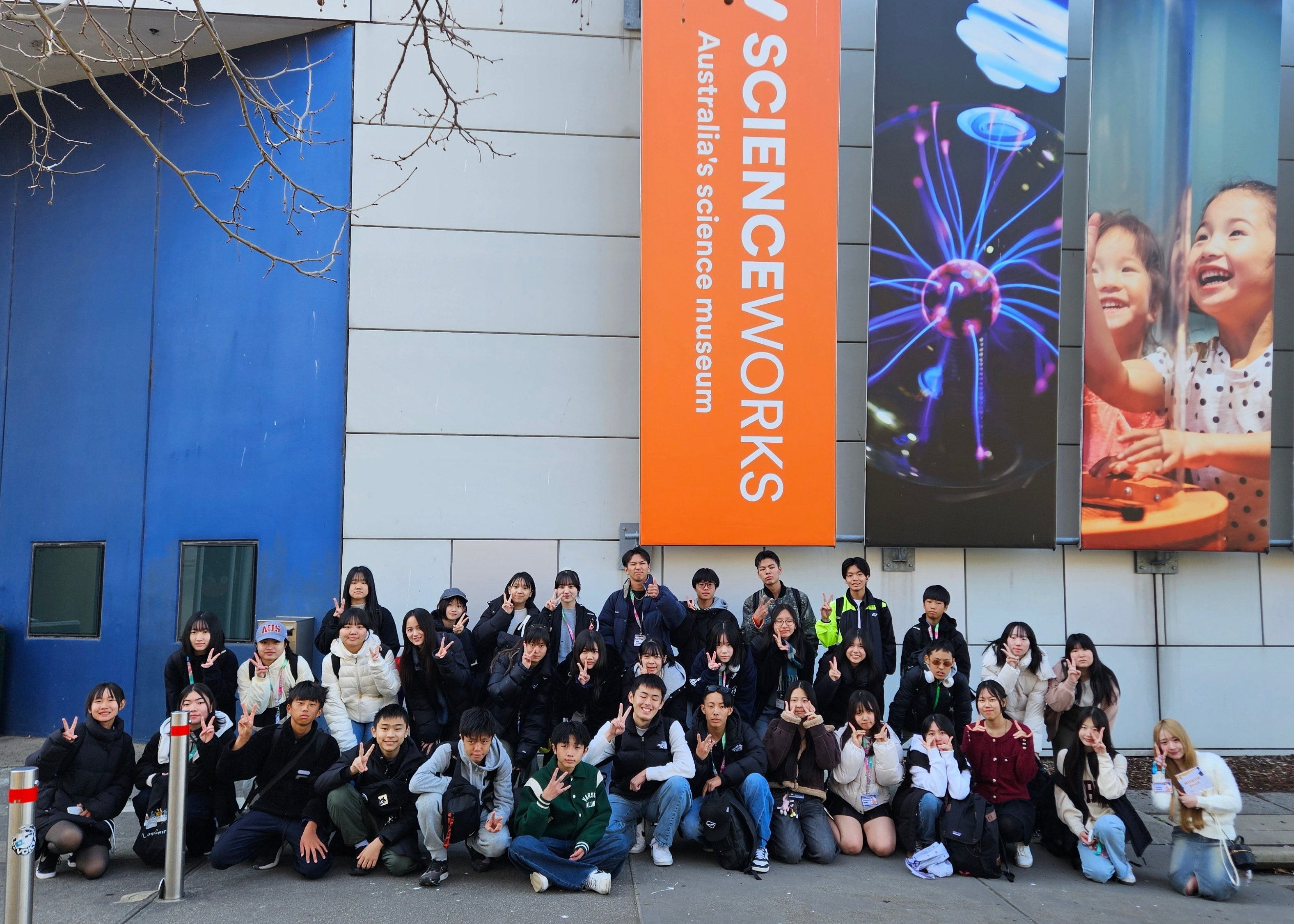 Group of people posing in front of Scienceworks building with large banners.