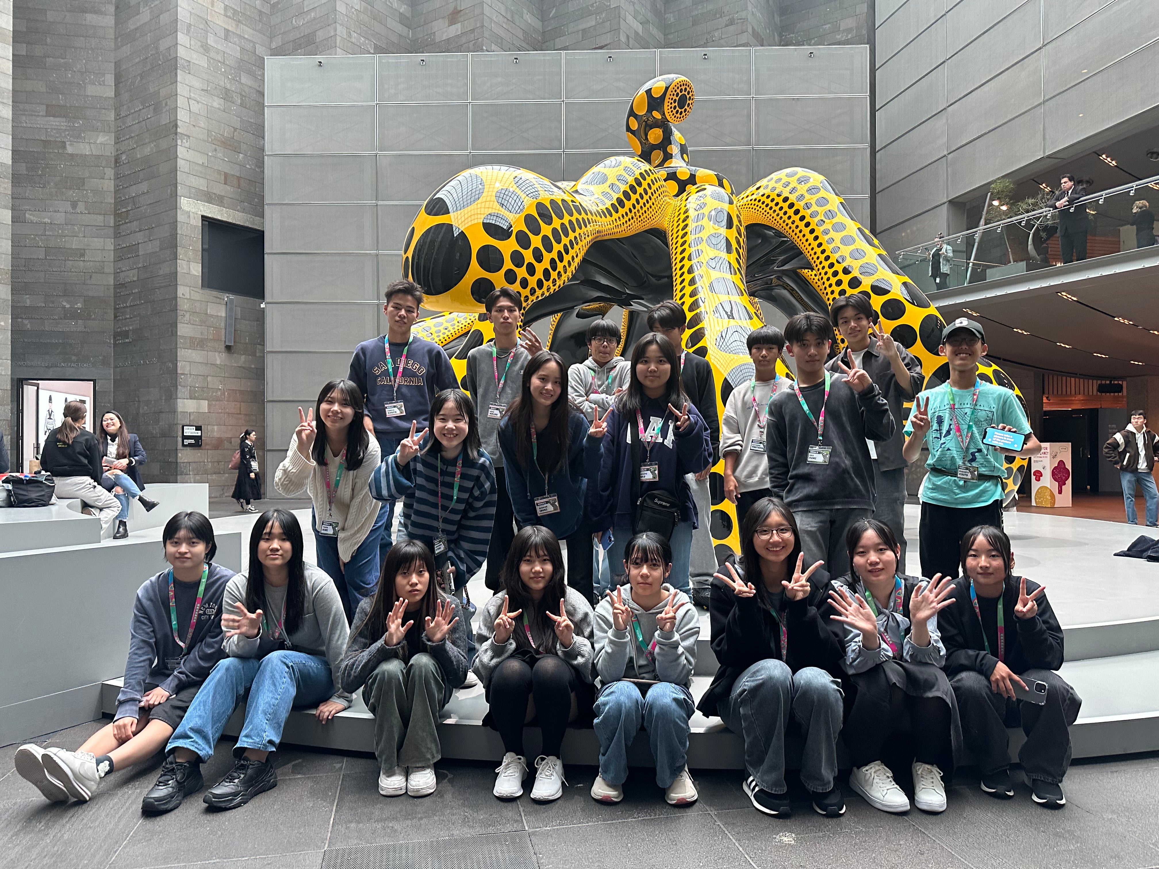 Group of people posing in front of a large, colorful sculpture of a dragon-like creature in an indoor setting.