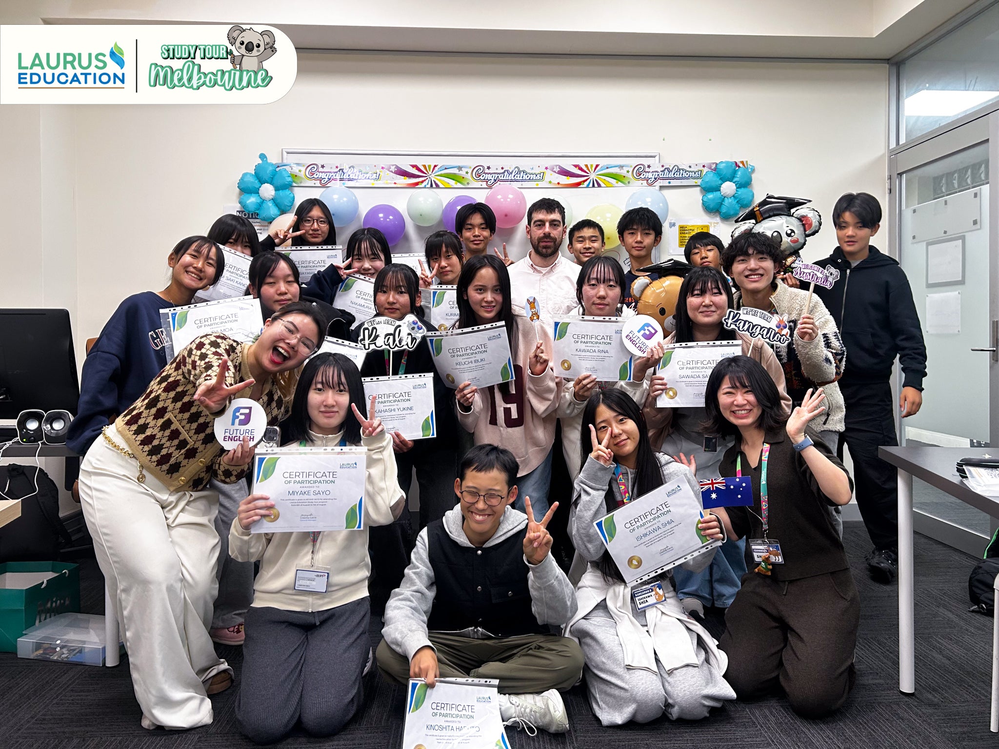 Group of people holding certificates in a room with balloons and a banner.