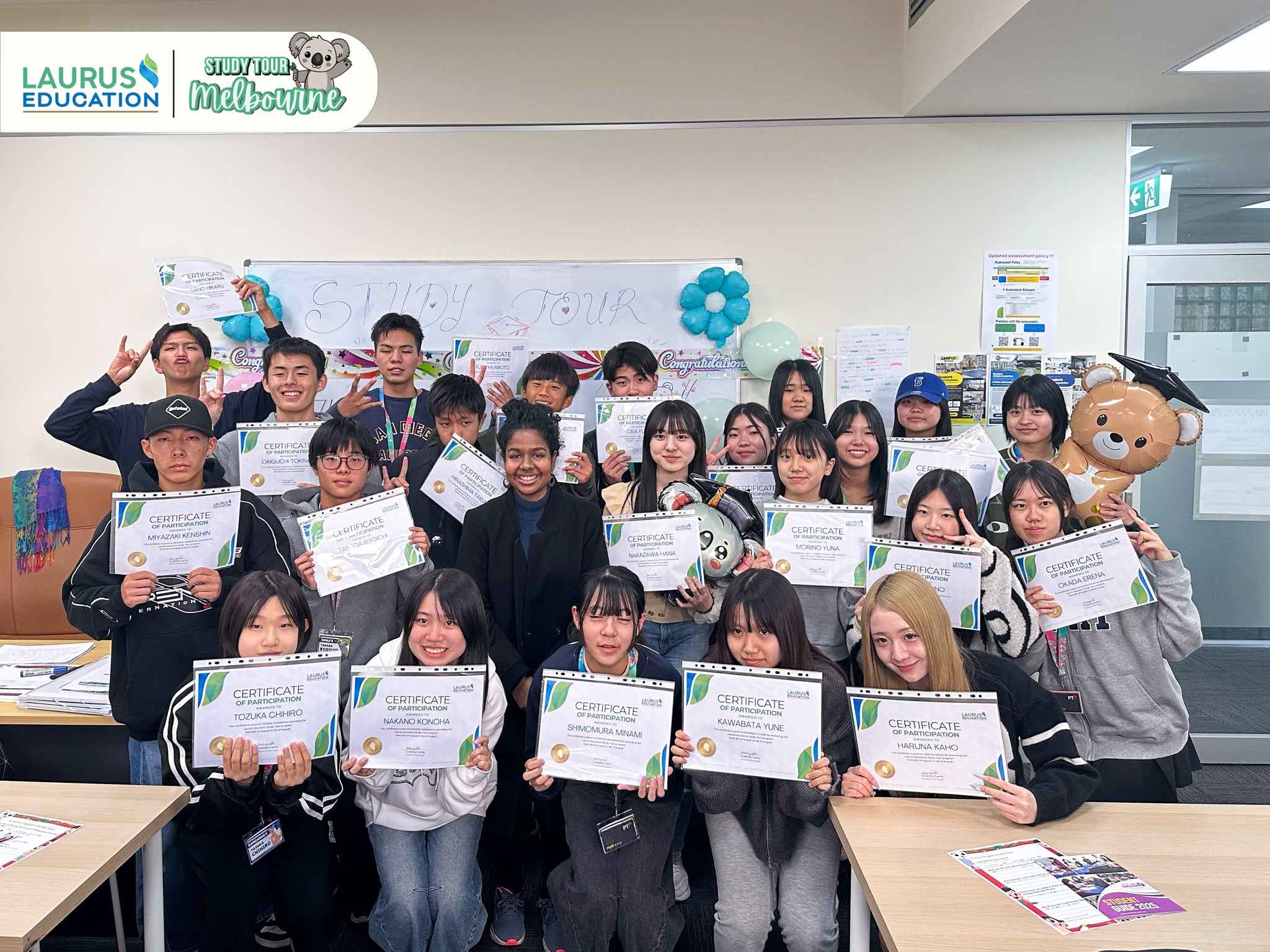 Group of students holding certificates in a classroom setting with educational posters on the wall.